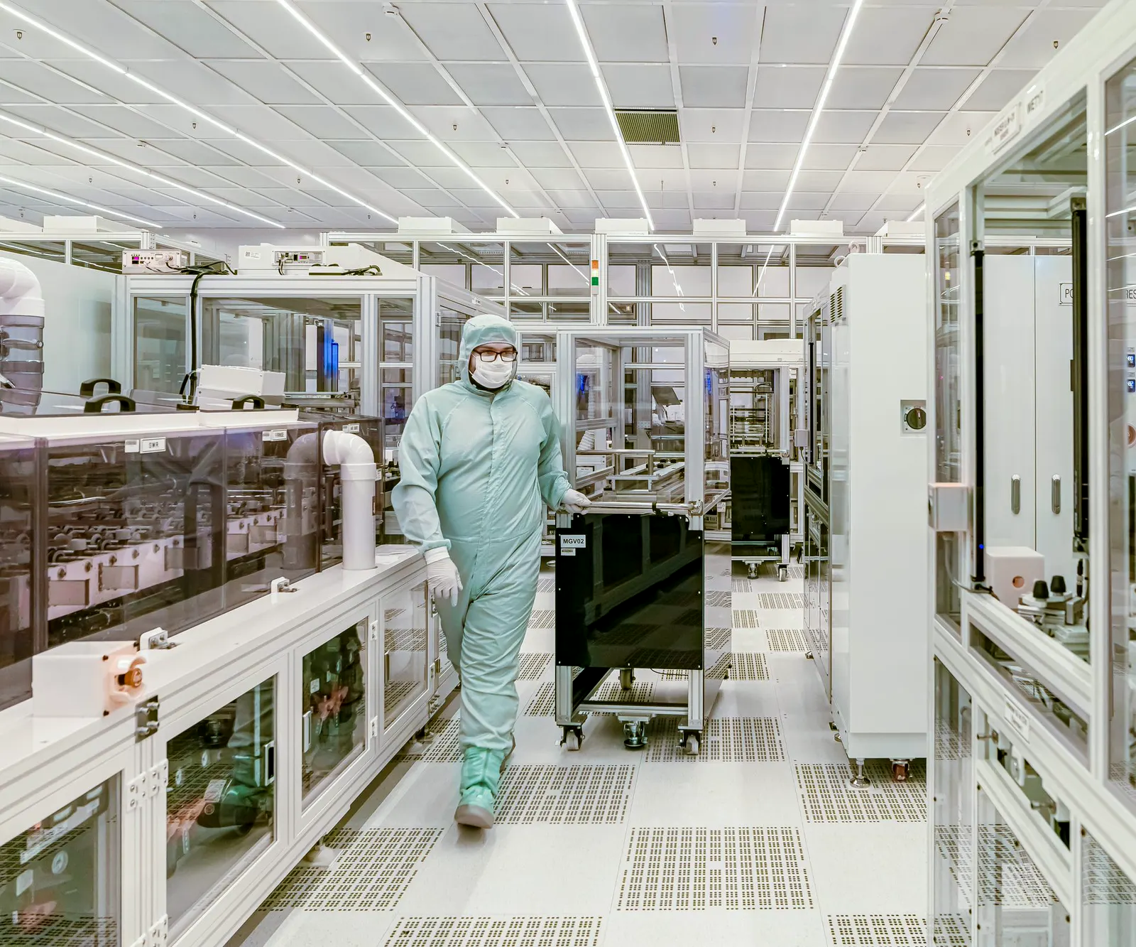 A technician in a cleanroom suit walking the aisle of a component fabrication facility.